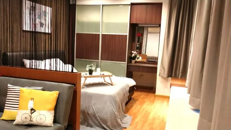 Room features: wooden flooring, grey bedspread, black upholstered headboard, decorative wall art, curtains, dressing table with mirror, wooden cabinetry, sofa with throw pillows, bedside table, table with decorative items; style: modern.