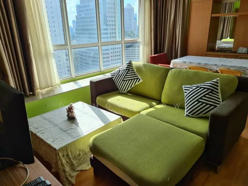 Living features: L-shape sectional sofa in green, coffee table with lace cover, floor-to-ceiling windows, curtains in beige, wooden flooring, decorative cushions with geometric pattern, TV console, dining table in background; style: modern; view: city.