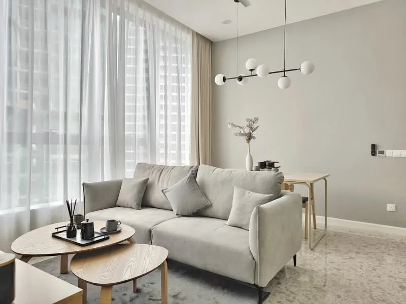 Living features: light grey fabric sofa, 2 decorative cushions, 2 round wooden coffee tables, black ceramic vase with dried flowers, set of black cups, minimalist pendant light with spherical bulbs, floor-to-ceiling windows with sheer curtains, neutral painted walls, carpeted flooring, wooden dining table with 2 chairs; style: modern; view: city.