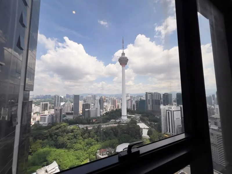 Exterior type: high-rise condominium; features: city skyline view, KL Tower visible, surrounded by greenery, modern glass facade, urban landscape, clear blue sky, clouds, high-rise buildings; style: modern.