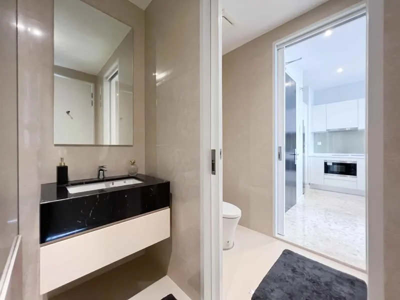 Bathroom features: single-sink vanity with black countertop, mirror above vanity, cream painted walls, tile flooring, toilet, glass door leading to adjacent room, recessed lighting, towel rail; style: modern. Room features: white cabinetry, built-in oven, microwave, kitchen countertop, tile flooring.