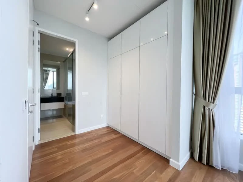 Room features: white painted walls, wooden flooring, built-in wardrobe with glossy finish, floor-to-ceiling windows, curtains in beige, recessed lighting, door leading to bathroom, neutral color scheme; style: modern.
