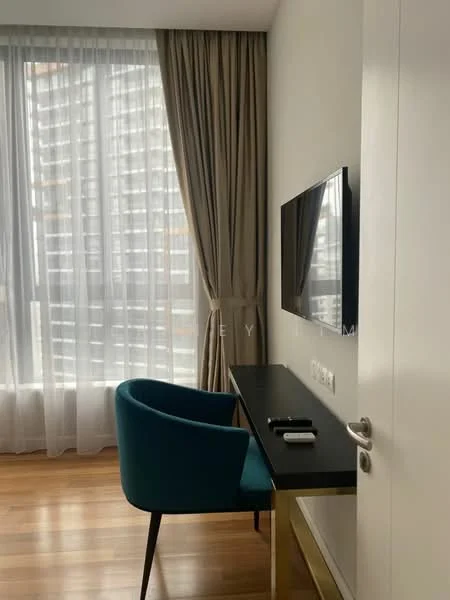 Room features: wooden flooring, floor-to-ceiling windows, sheer curtains, dark blue upholstered chair, wall-mounted TV, desk with metallic legs, remote control on desk, neutral wall color; style: modern.