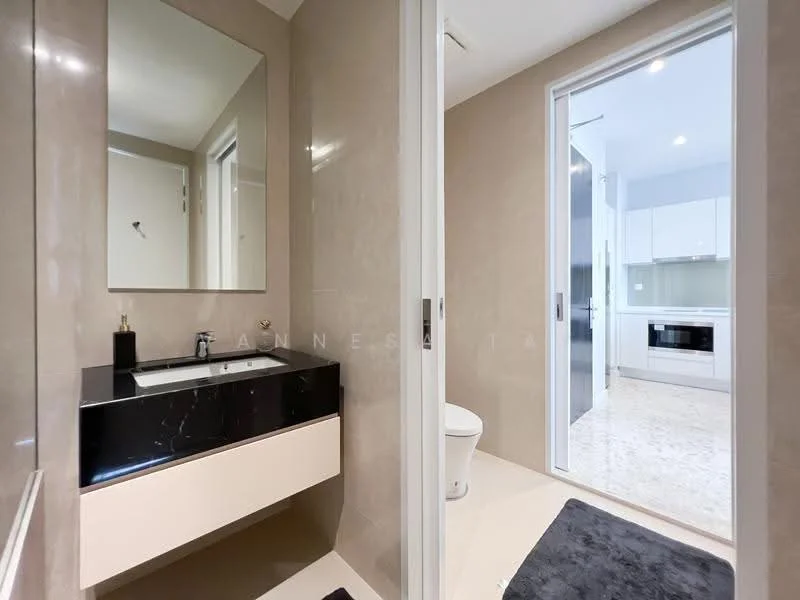 Bathroom features: black countertop with sink, wall-mounted faucet, mirror above sink, cream cabinetry, white toilet, light-colored wall tiles, marble flooring, sliding door to adjacent room; style: modern. Room features: white cabinetry, built-in oven, kitchen countertop, light-colored wall tiles, marble flooring.