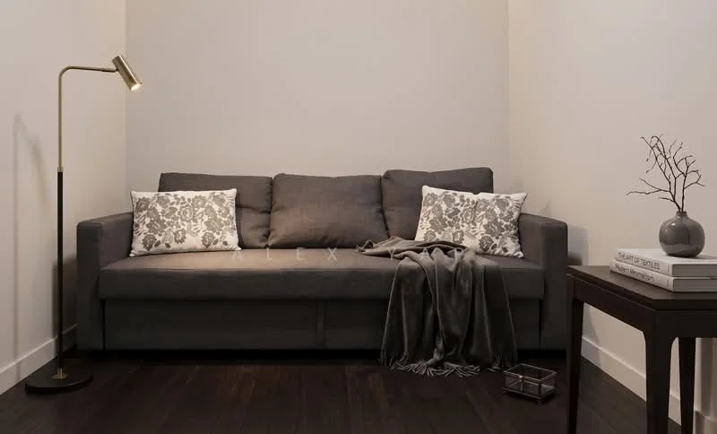 Living features: grey fabric sofa, decorative throw pillows with floral pattern, floor lamp with gold finish, wooden side table, decorative vase, throw blanket, dark hardwood flooring, neutral painted walls; style: modern.