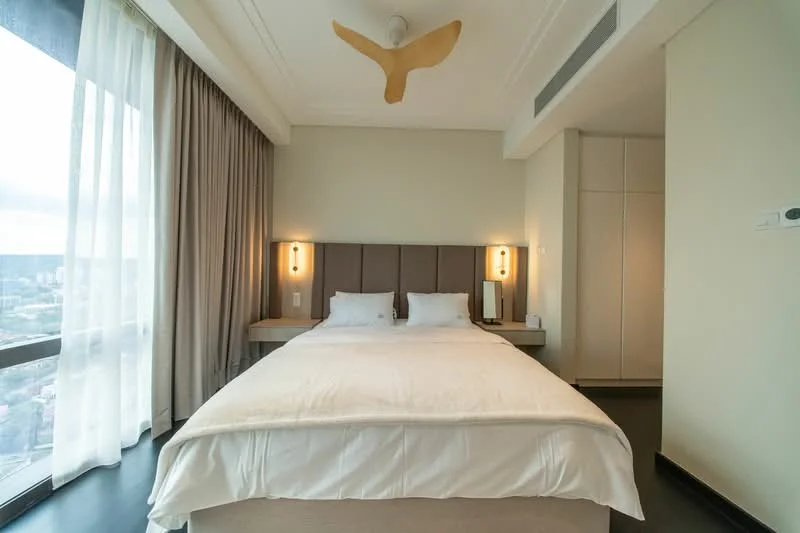 Bedroom features: king-size bed with white bedding, upholstered headboard, two bedside lamps, floor-to-ceiling windows, sheer curtains, wooden flooring, decorative ceiling feature, built-in wardrobe, wall-mounted light fixtures; style: modern; view: city.
