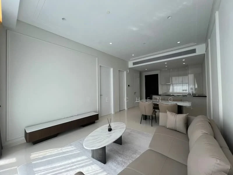 Living features: light beige fabric sofa, marble coffee table, white walls, recessed downlights, large windows with sheer curtains, flat-panel TV console in dark wood, area rug with neutral tones, open layout to kitchen, high ceiling; style: modern. Room features: white painted walls, light-colored flooring, kitchen area visible in background.