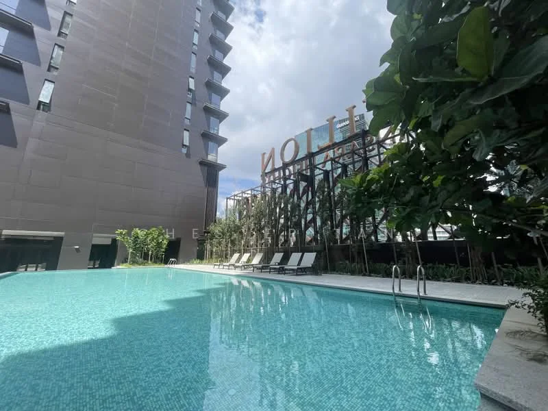 Exterior type: high-rise condominium; features: infinity pool, pool deck with loungers, landscaped greenery, glass curtain wall facade, signage with the word 'HILTON', manicured landscaping, surrounded by tropical plants; style: modern.
