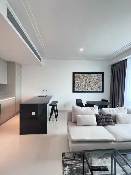 Living features: white painted walls, light-colored flooring, sofa with multiple cushions, glass coffee table, area rug with geometric pattern, wall-mounted artwork, floor-to-ceiling windows with sheer curtains, recessed downlights, open kitchen layout, black kitchen island with bar stools, dining table with black chairs; style: modern.