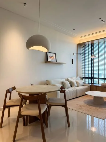 Living features: white painted walls, polished marble flooring, large floor-to-ceiling windows with blinds, sofa with multiple cushions in light color, round coffee table, 6-seater dining table with wooden legs, upholstered dining chairs, pendant light fixture, wall-mounted shelf with framed artwork, decorative area rug; style: modern; view: city.