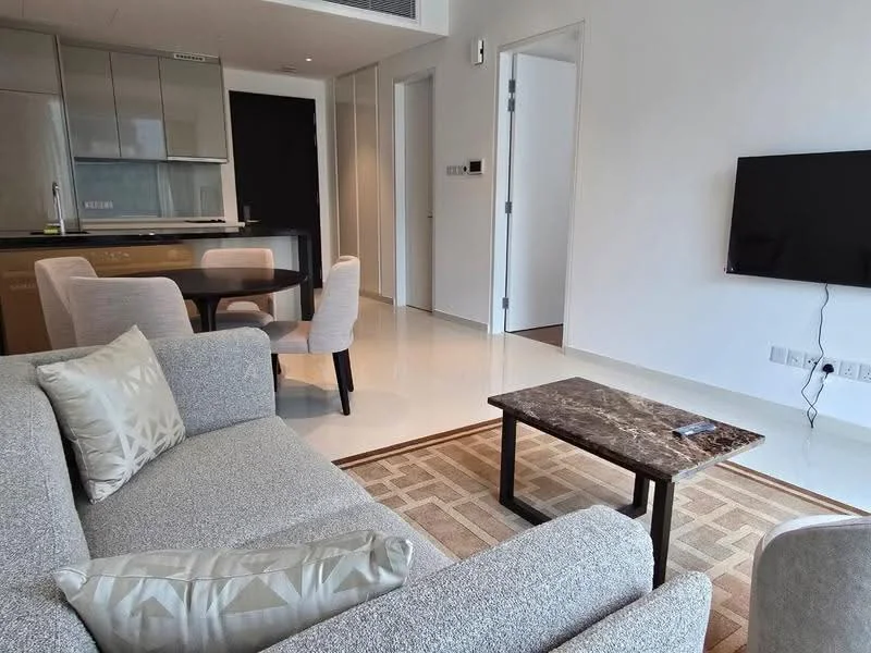 Living features: light grey fabric sofa, decorative cushion with geometric pattern, marble coffee table, area rug with geometric pattern, wall-mounted TV, white painted walls, recessed downlights, open-plan layout with kitchen and dining area visible, glossy tiled flooring; style: modern. Dining features: 4-seater dining table, upholstered dining chairs, open layout to living area; style: modern. Kitchen features: kitchen cabinetry with glossy finish, built-in appliances, countertop with bar seating, open layout to living area; style: modern.