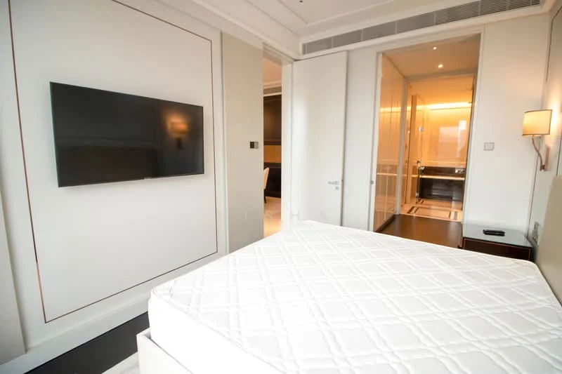 Bedroom features: queen-size bed base, wall-mounted flat-screen TV, white painted walls, recessed downlights, wooden bedside table, wall sconce, sliding door to adjoining room, carpet flooring; style: modern.