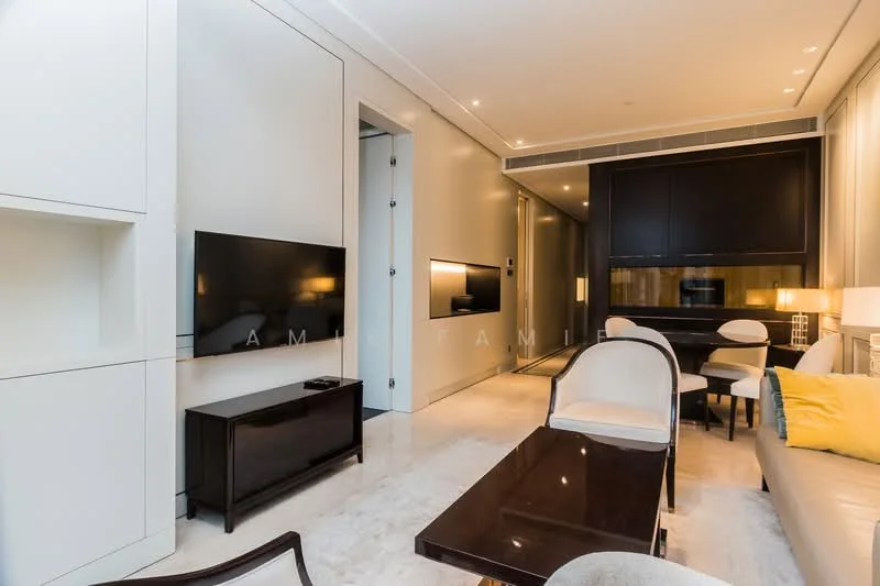 Living features: cream painted walls, marble flooring, wall-mounted TV, dark wood console table, light-colored upholstered chairs, dark wood coffee table, recessed downlights, sofa with yellow accent pillows, dining area visible in background, built-in cabinetry, neutral color palette; style: modern.
