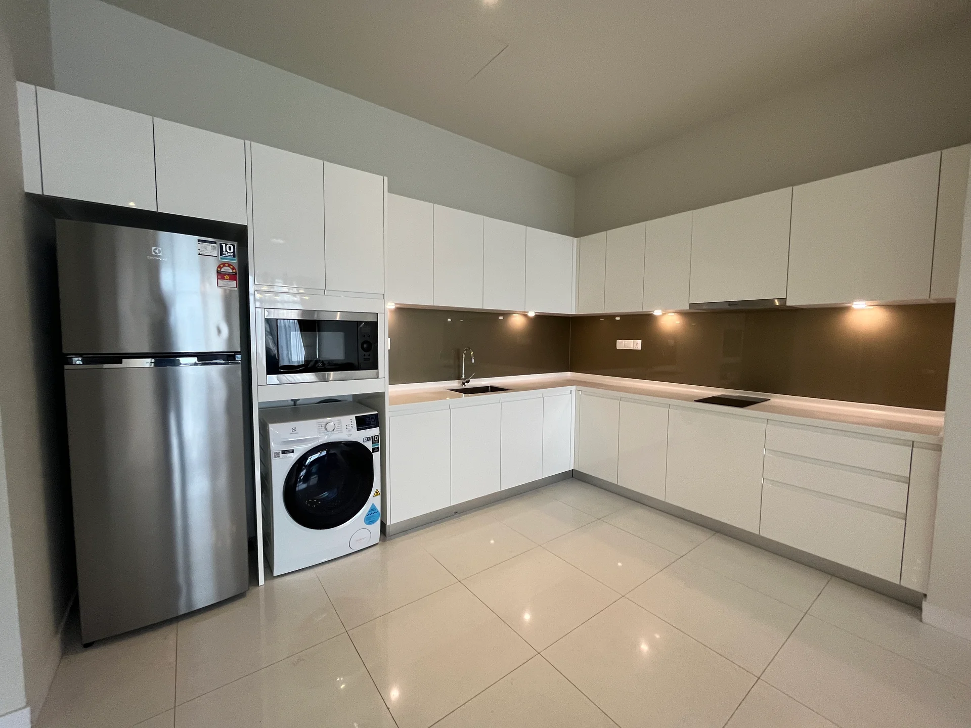 Kitchen features: white flat-panel cabinets, stainless-steel fridge, built-in microwave, white countertop, glass backsplash, stainless-steel sink, chrome pull-down faucet, built-in induction hob, front-load washing machine, recessed LED downlights, ceramic tile flooring, neutral wall color; style: modern.