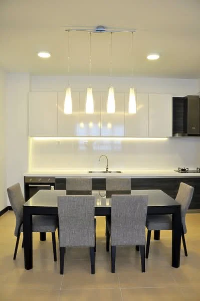 Dining features: 6-seater dining table, black glass tabletop, upholstered dining chairs in grey, pendant lighting with three fixtures, white cabinetry with glossy finish, black lower cabinetry, stainless-steel sink, chrome faucet, built-in gas hob, recessed LED downlights, cream tiled flooring, white backsplash; style: modern.