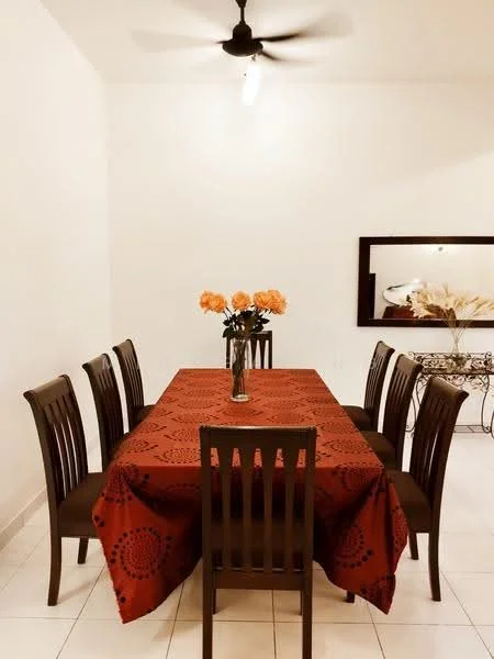 Dining features: 6-seater dining table, dark wood dining chairs, red tablecloth with circular pattern, vase with orange flowers, white painted walls, ceiling fan, mirror on wall, decorative console table; style: modern.