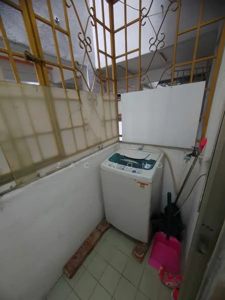 Laundry features: top-load washing machine, white exterior, tile flooring, grey walls, window with metal grille, plastic bucket, cleaning supplies, drainage hose.