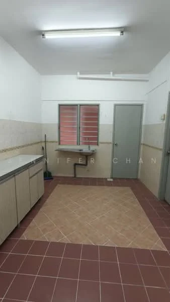 Kitchen features: laminate cabinetry in light wood, white tiled walls, brown tiled flooring, single-bowl stainless-steel sink, chrome faucet, window with red shutters, door to hallway, cleaning supplies storage area, fluorescent ceiling lights.