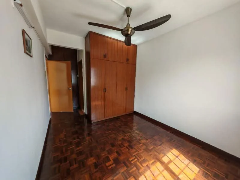 Bedroom features: parquet wood flooring, white painted walls, ceiling fan with 3 blades, built-in wooden wardrobe, door leading to hallway, natural light from window.