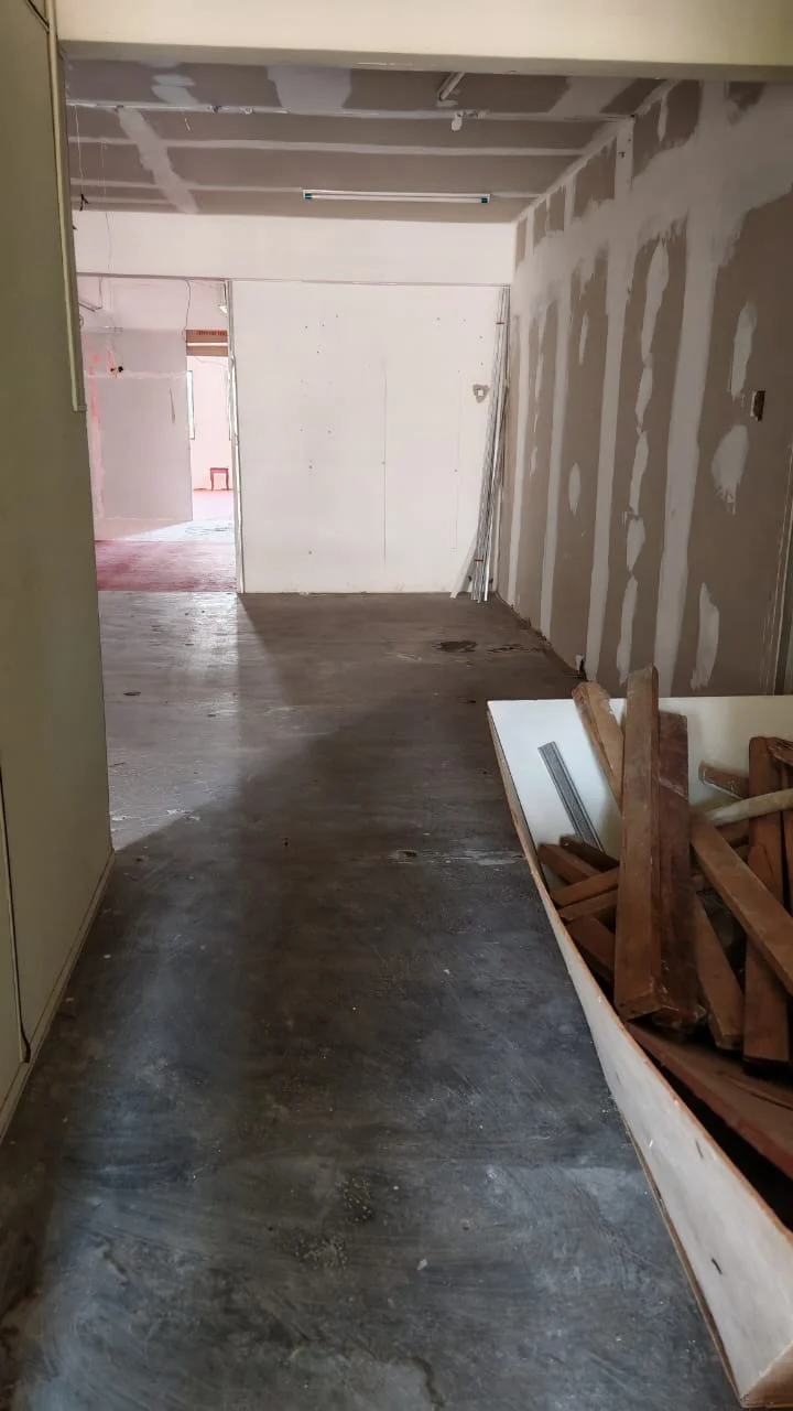 Room features: unfinished walls with drywall, concrete flooring, exposed ceiling, debris including wooden planks, open layout, natural light from doorway, no visible fixtures or furnishings.