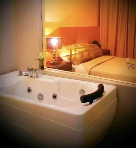 Bathroom features: freestanding bathtub, chrome faucet, built-in jets, mirror, soft lighting, decorative lamp, curtains, wooden accent wall; style: modern.