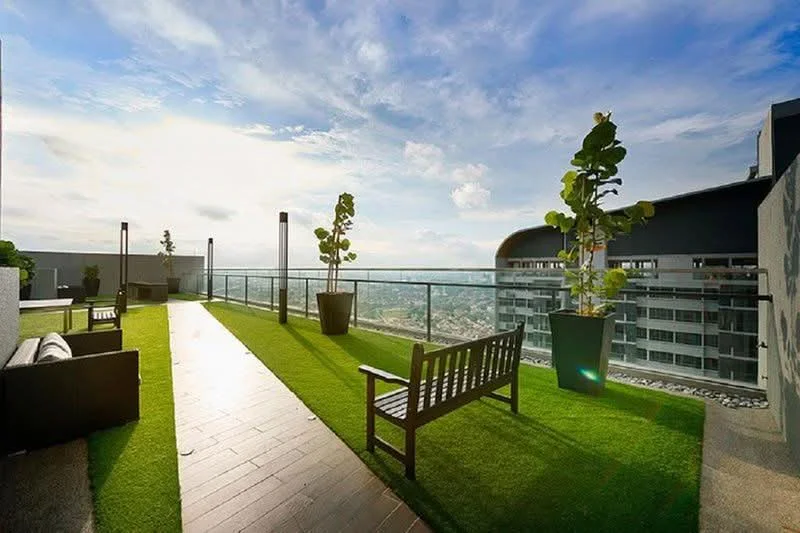 Exterior type: rooftop garden; features: artificial grass lawn, concrete pathway, glass railing, outdoor seating area with benches, potted plants, city skyline view, sunny weather, modern architectural elements; style: modern.