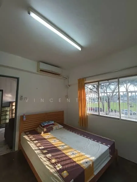Bedroom features: single bed, wooden bed frame, mattress with white bedding, decorative throw blanket, window with white curtains, air conditioning unit, light fixture with fluorescent tube, painted walls in white, concrete flooring, built-in wardrobe, view of outdoor greenery; view: garden.