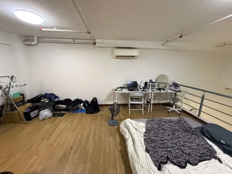 Room features: wooden flooring, white painted walls, exposed ceiling with pipes, 1 wall-mounted split AC, desk with computer and mirror, white folding chairs, bed with bedding, fan, clothing on the floor, storage boxes; style: minimalist.