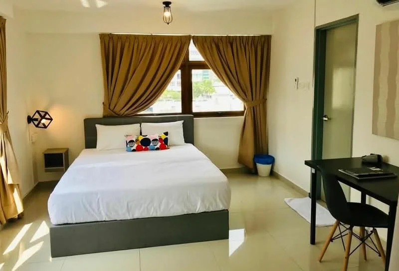 Bedroom features: queen-size bed with white bedding, decorative pillow with colorful pattern, floor-to-ceiling window with brown curtains, light fixture with exposed bulb, grey upholstered bed frame, white tiled flooring, small nightstand, black study desk, black chair, waste bin, white bath mat, wall-mounted air conditioning unit; style: modern; view: city.