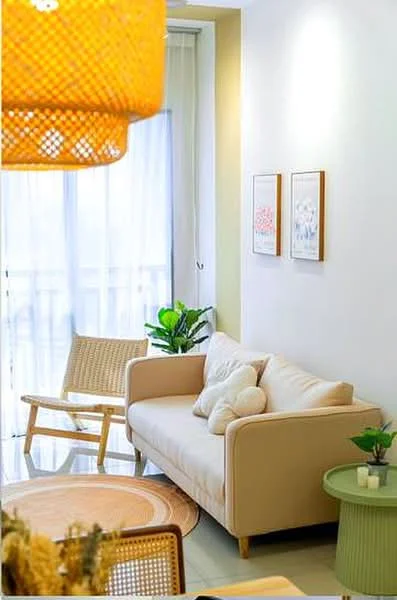Living features: beige fabric sofa, round area rug, wooden rocking chair, green side table, framed artwork on walls, floor-to-ceiling windows with sheer curtains, indoor plants, pendant light fixture; style: modern.