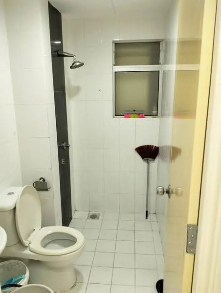 Bathroom features: white tiled walls, white tiled flooring, one-piece toilet, shower with wall-mounted faucet, glass shower enclosure, small window, toilet paper holder, broom, drain in floor.