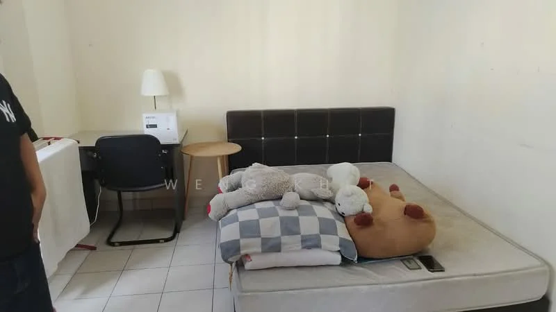 Bedroom features: queen-size bed, black upholstered headboard, mattress on bed frame, white bedding, two large pillows, stuffed animals on bed, desk with chair, table lamp, wooden side table, white wall, tile flooring.
