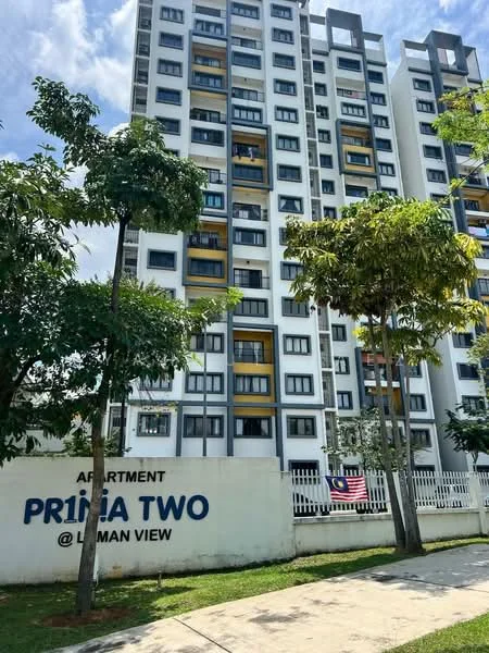 Exterior type: mid-rise condominium; features: white painted facade, grey accent panels, balconies with yellow accents, multiple storeys, landscaped garden area, surrounding trees, fenced perimeter, visible Malaysian flag, signage with building name, concrete pathway; style: modern.