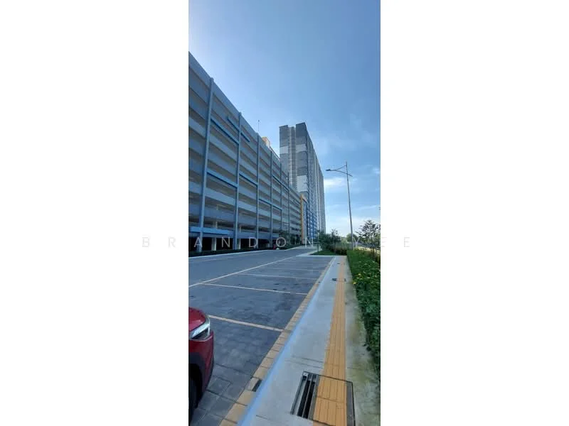 Exterior type: mid-rise condominium; features: grey concrete facade, multiple storeys, open-air parking lot, landscaped area with greenery, street lighting, paved walkway, adjacent to road; style: modern.