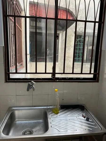 Kitchen features: stainless-steel sink, chrome faucet, window with security bars, white tiled walls, grey tiled flooring, countertop with drainage grooves, bottle of dish soap, black kitchen utensil, visible plumbing, natural light from window.