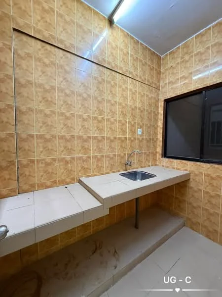 Kitchen features: single-bowl stainless-steel sink, chrome faucet, light-colored tiled backsplash, orange patterned wall tiles, white countertop, built-in countertop with extended section, window with black frame, light fixture on ceiling, flooring with light-colored tiles.