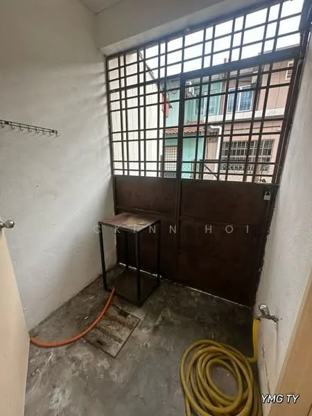 Room features: concrete flooring, white painted walls, metal security grille door, small table, hose pipe, wall-mounted shelf, exposed plumbing, natural light from window.