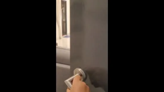 Room features: grey painted walls, metal door handle, door frame, visible flooring, interior door, light source in background.