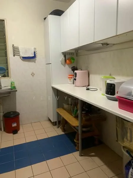 Kitchen features: white cabinetry, countertop with white surface, pink kettle, black rice cooker, white microwave, stainless-steel sink, wall-mounted shelf, tile flooring in beige and blue, window with metal grille, wooden bench, trash bin, green dish soap, cleaning cloth, cooking utensils.