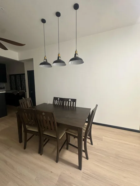 Dining features: 6-seater dining table, wooden dining chairs, pendant lighting with three fixtures, light wood flooring, white painted walls, ceiling fan, open layout to kitchen, neutral color scheme; style: modern.