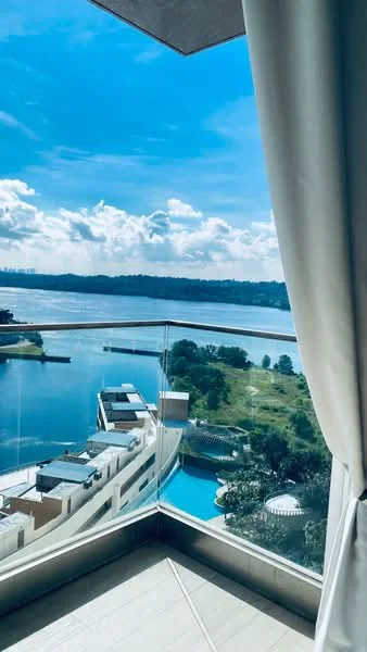 Room features: floor-to-ceiling windows, glass balcony railing, curtains, view of water, view of landscaped area, view of swimming pool, blue sky, clouds; style: modern; view: water.