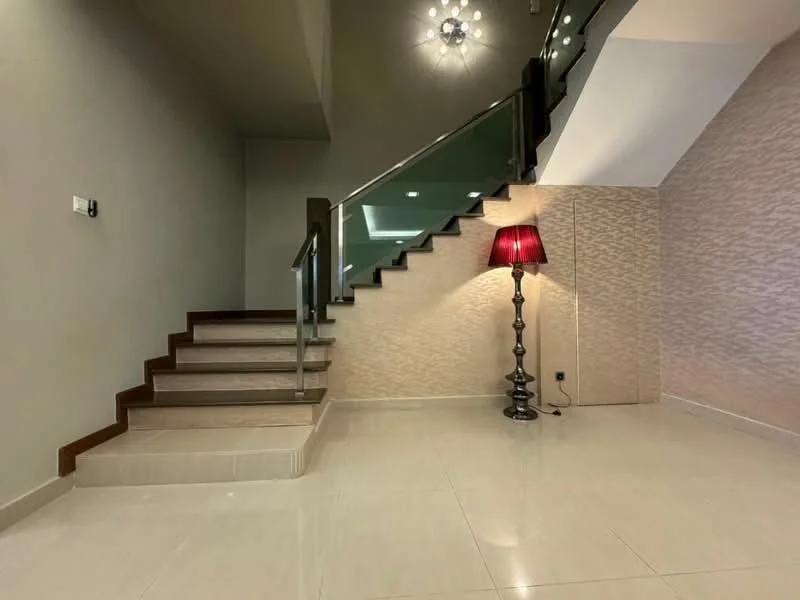 Room features: staircase with wooden steps, glass railing, wall-mounted light switch, recessed ceiling lights, chandelier with multiple bulbs, cream painted walls, textured wallpaper, polished ceramic tile flooring, decorative floor lamp with red shade; style: modern.