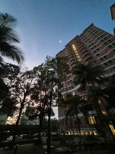 Exterior type: high-rise condominium; features: red brick facade, approximately 15-storey high-rise, surrounded by mature trees, landscaped garden area, night lighting on building, balconies on upper floors, parking area visible in foreground; style: modern.