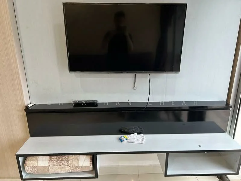 Living features: wall-mounted TV, black TV console, white shelving unit, light-colored wall, glossy floor tiles, remote control on console, black decorative item on console, towel on shelf; style: modern.