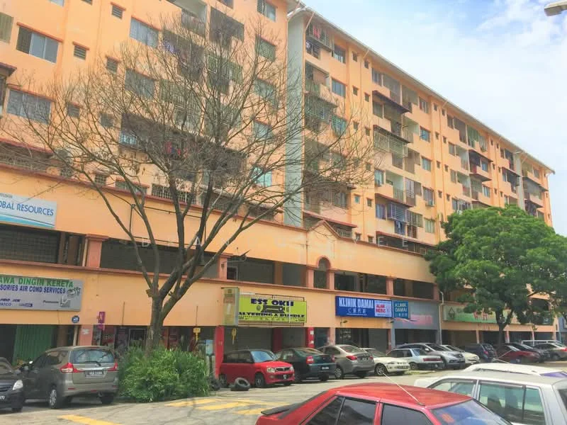 Exterior type: low-rise apartment block; features: orange painted facade, multiple storeys, commercial spaces on ground floor, parking area in front, trees in landscaping, clear blue sky, visible signage for businesses; style: modern.