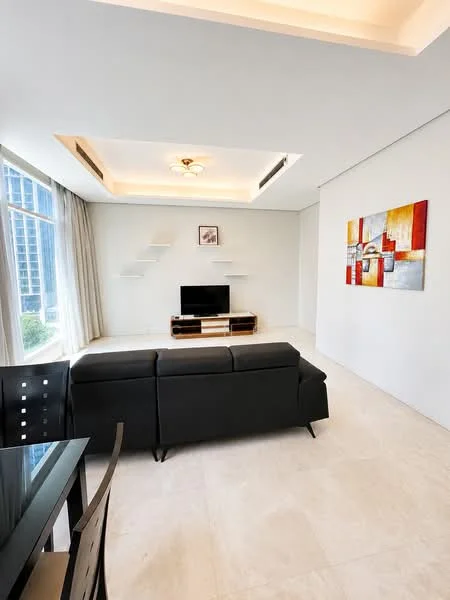 Living features: black leather sofa, wall-mounted TV, wooden TV console, white painted walls, recessed ceiling with lighting, large floor-to-ceiling windows, sheer curtains, decorative wall art, cream tile flooring; style: modern; view: city.