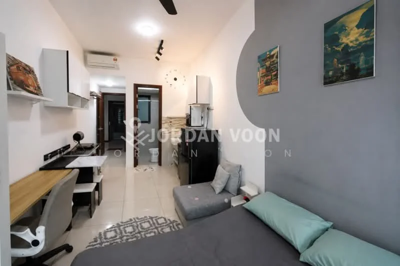 Room features: queen-size bed with grey bedding, sofa in light grey fabric, study desk with wooden surface, white office chair, wall-mounted air conditioning unit, recessed ceiling lights, floor tiles in white, decorative wall art, framed artwork on walls, small refrigerator, kitchenette with sink, open shelving, clock on wall, window with natural light; style: modern.