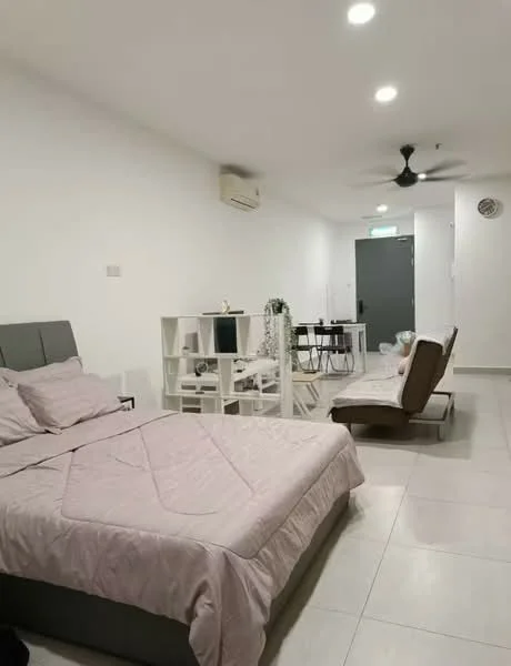 Room features: queen-size bed with grey upholstered headboard, light pink bedding, white painted walls, tile flooring, 5-blade ceiling fan, 1 wall-mounted split AC, dining table for 2, white open shelving unit, brown fabric sofa bed, decorative plants, wall-mounted light fixture, door with security lock, window with no visible treatment; style: modern.