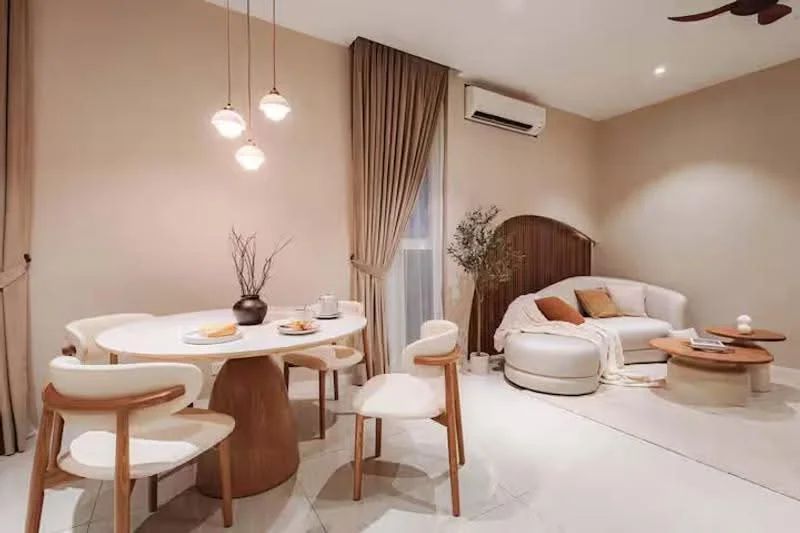 Dining features: round dining table, 4 wooden dining chairs, decorative vase with branches, table setting with plates and cups, light-colored table surface, wooden pedestal base, soft beige wall color, recessed downlights; style: modern. Living features: curved white sofa, wooden coffee table, decorative items on coffee table, beige area rug, floor-to-ceiling window with sheer curtains, wall-mounted air conditioning unit, ceiling fan, soft lighting from pendant lights; style: modern.