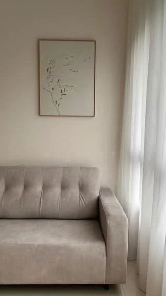 Living features: light grey fabric sofa, framed artwork on wall, white sheer curtains, light-coloured walls, neutral flooring, natural light from window; style: modern.